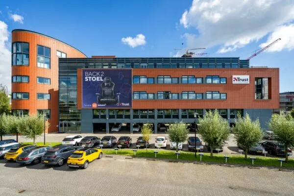 Modern kantoorgebouw aan de Laan van Barcelona met een groot reclamebord van Trust en geparkeerde auto's op de voorgrond.